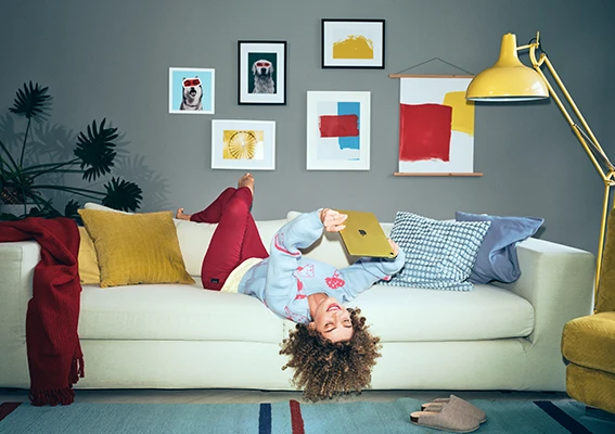 Bleib inspiriert – mit dem ORWO Newsletter auf deinem Tablet Junge Frau liegt auf der Couch und liest auf einem Tablet, umgeben von farbenfroher Einrichtung.