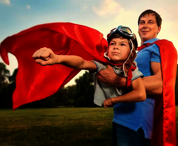Starke Familienmomente verschenken Vater und Kind im Superhelden-Outfit mit roten Umhängen im Freien als symbolisches Motiv für starke Familienmomente und persönliche Fotogeschenke zu besonderen Anlässen