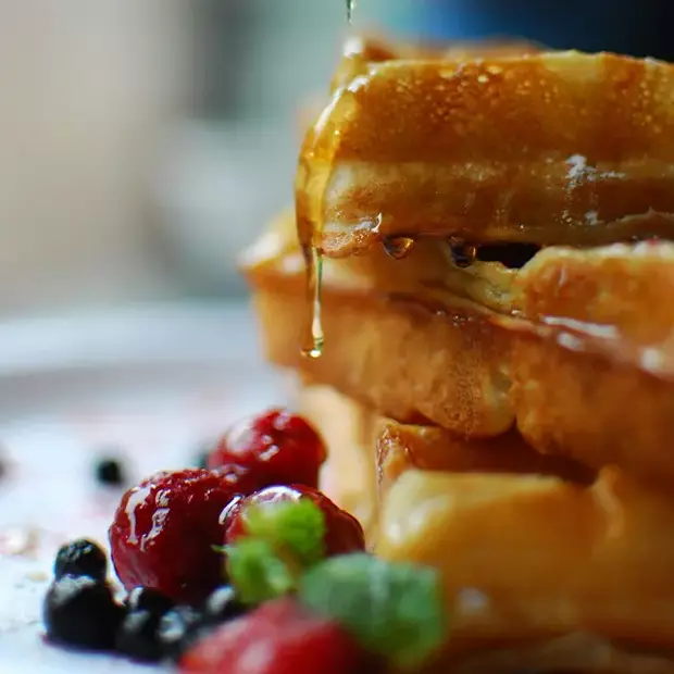 Hochwertige Bilder von Essen machen: Fotografiere eine detaillierte und superlecker aussehende Nahaufnahme eines Waffel-Desserts mit schmackhaften Beeren.