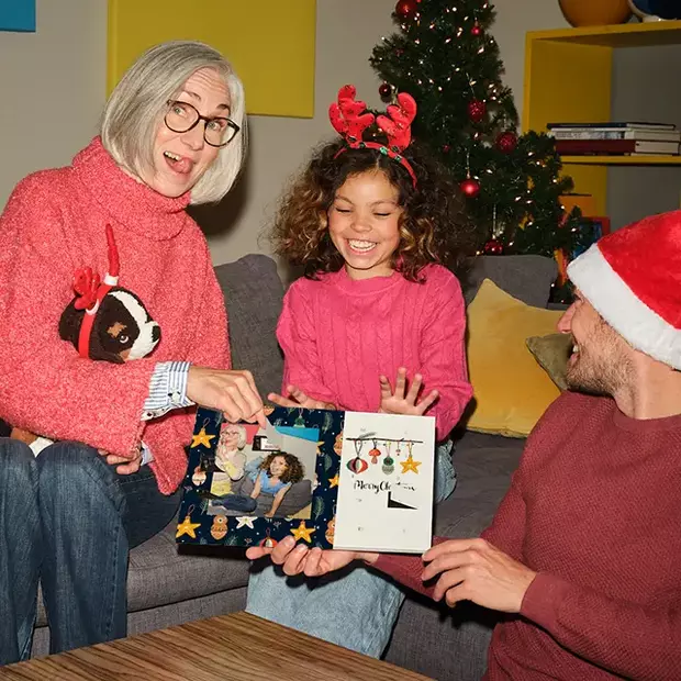 In gemütlicher Runde freuen sich Oma, Kind und Papa über einen liebevoll gestalteten Foto-Adventskalender und teilen festliche Momente mit Fotogeschenken zu Weihnachten.