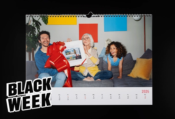 Fotokalender im Black Week Deal – individuelles Geschenk Individueller Fotokalender für das Jahr 2026 mit fröhlicher Familie auf dem Sofa, dekoriert mit großer roter Schleife, beworben als Black-Week-Sonderangebot.