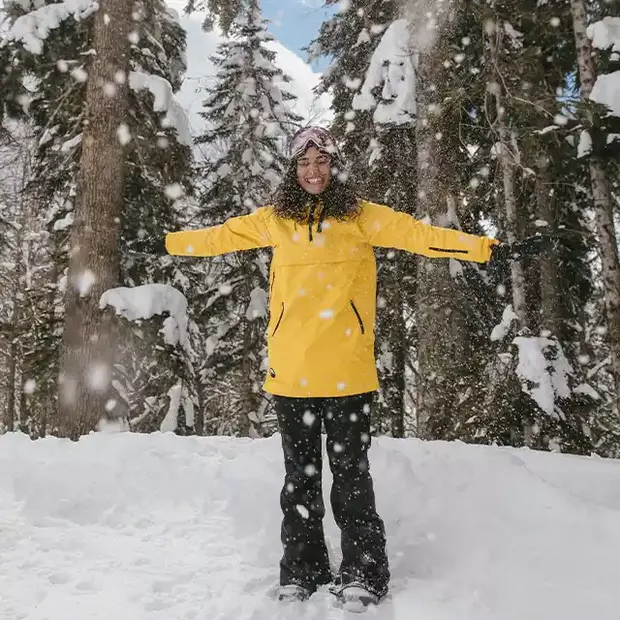 Eine Frau mit einer gelben Skijacke steht inmitten von Schneeflocken. Beim Fotografieren im Schnee können einzigartige Aufnahmen entstehen.