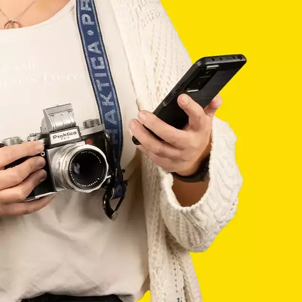 Eine Person informiert sich per Smartphone über die Funktionen ihrer Analogkamera, während sie sie in der Hand hält.