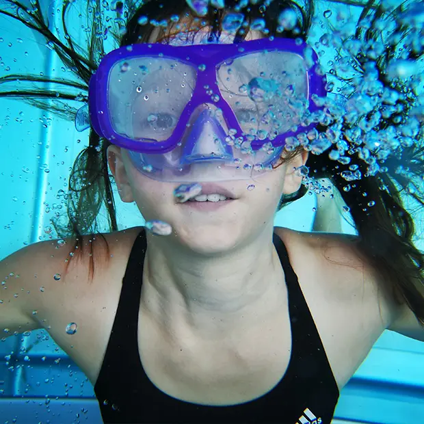 Ein Mädchen taucht mit Tauchermaske im Pool unter Wasser, Luftblasen steigen auf, ORWO gibt dir 10 Tipps wie du gut und sicher in die Unterwasserfotografie einsteigst.