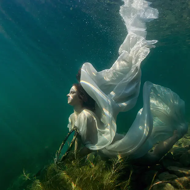 Sonnenlicht fällt in Strahlen auf eine schöne Frau im weißen Kleid unter Wasser, auch Modelfotos unter Wasser gelingen mit den Tipps von ORWO zur Unterwasserfotografie.