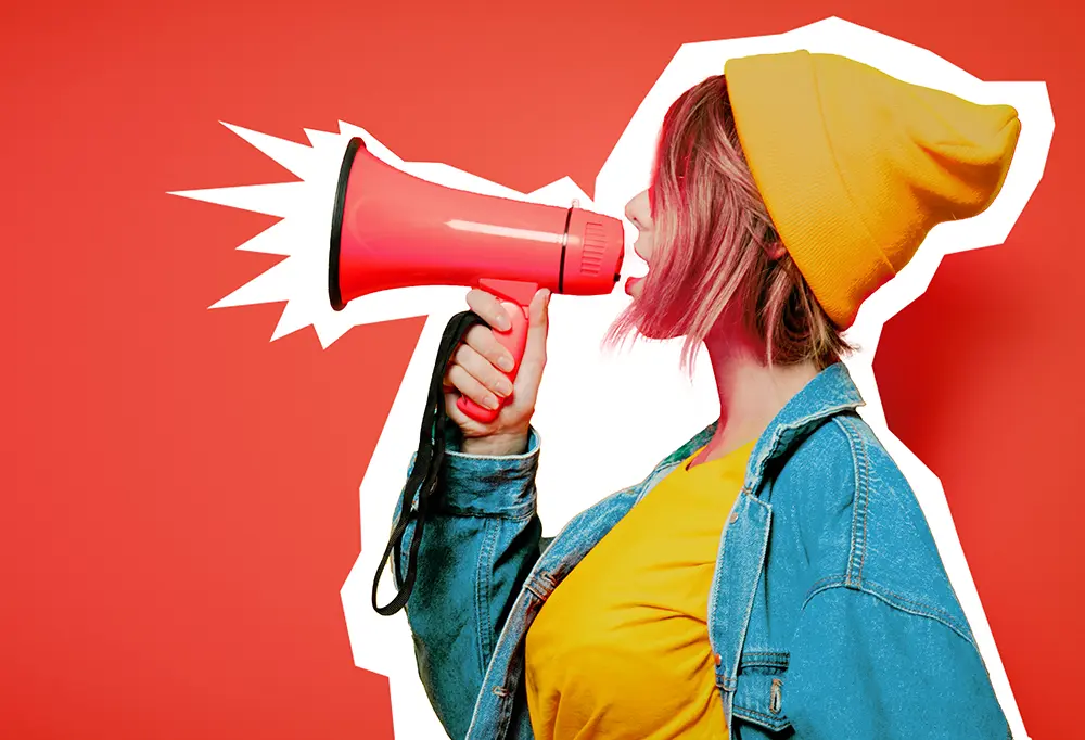 Neue Fotoprodukte mit Stil vorstellen Eine bunt gekleidete Frau hält ein Megafon und präsentiert begeistert die neuen Fotoprodukte. Das Bild sprüht vor Farben und Energie, was die lebendige Atmosphäre und die Vielfalt der angebotenen Fotoprodukte unterstreicht.