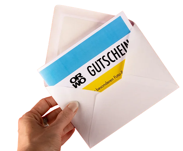 ORWO Geschenkgutschein – das perfekte Geschenk für kreative Fotoprojekte Hand hält weißen Umschlag mit ORWO Geschenkgutschein in Blau und Gelb.