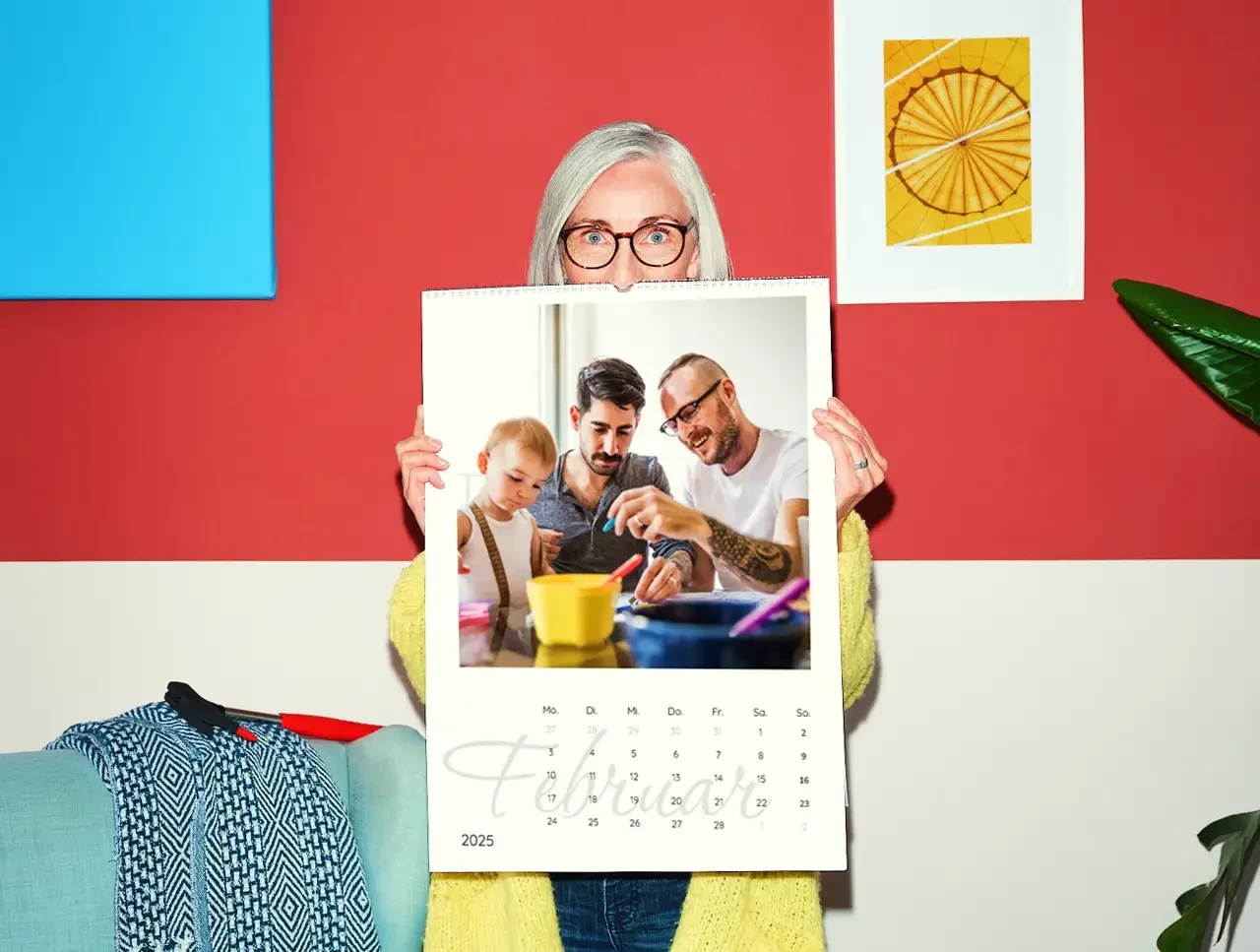 Eine weißhaarige Frau im gelben Strickmantel hält einen großen Terminkalender vor sich, der zeigt, wie du deinen Fotokalender selbst gestalten könntest.