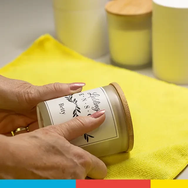 Zwei Hände kleben sorgsam das personalisierte Etikett auf das Glas einer Kerze mit Foto auf.